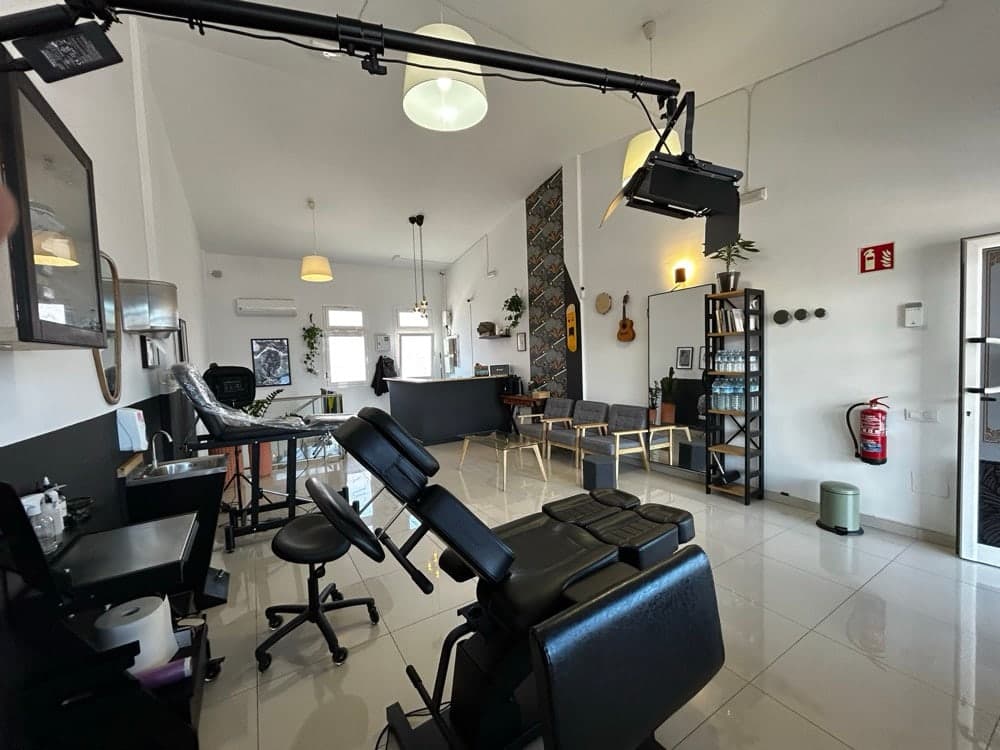 Inside the studio: a black tattoo chair and workstation in a bright white room.