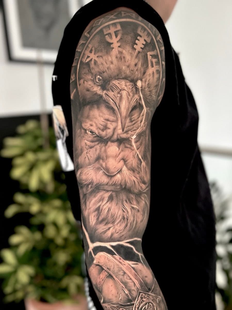 Black and grey Odin with a raven perched above and runes behind, on the upper arm.