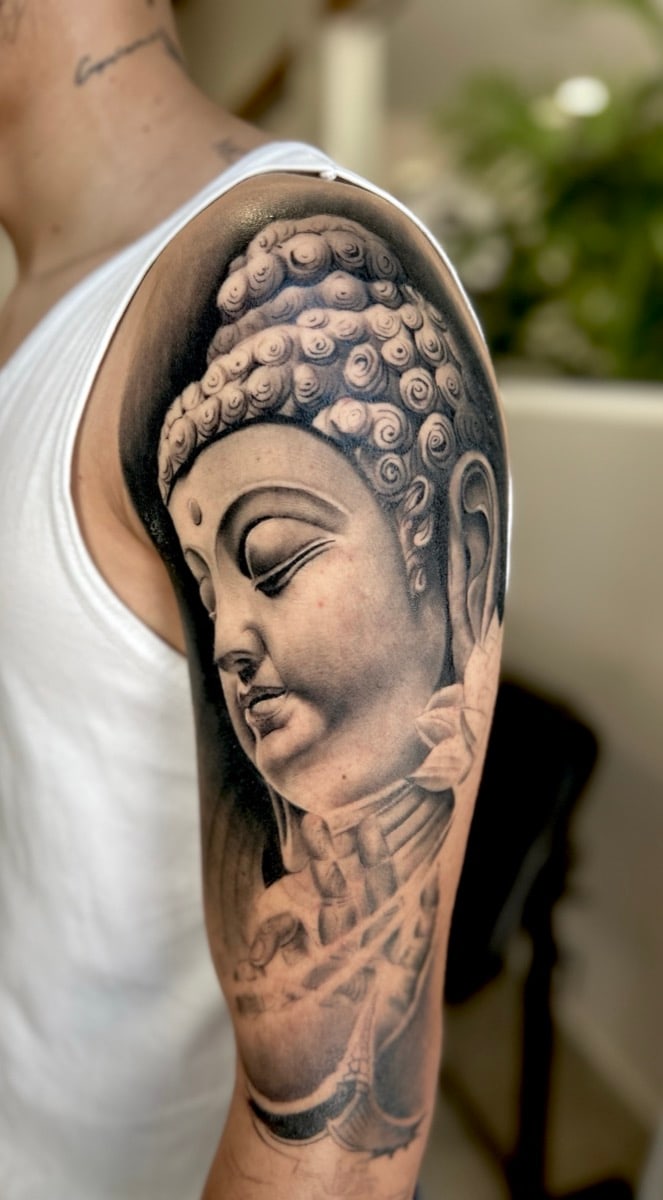 Black and grey Buddha with closed eyes, on the upper arm and shoulder.